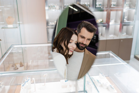 Smiling couple reflecting in mirror of jewelry shopの写真素材