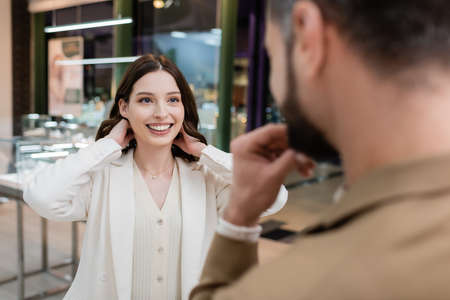Positive woman wearing necklace near blurred boyfriend in jewelry shopの写真素材