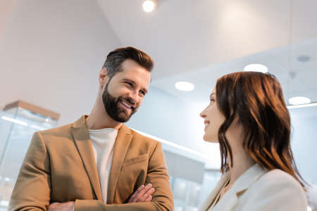 Smiling man with crossed arms looking at girlfriend in jewelry storeの写真素材