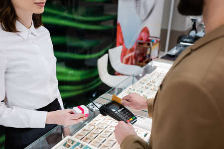 Cropped view of seller holding gift near customer paying with credit card in jewelry shop