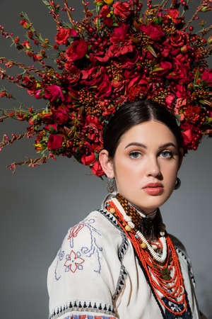 portrait of pretty ukrainian woman in traditional clothing and floral red wreath isolated on greyの写真素材