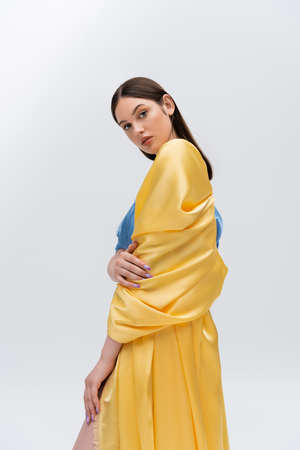 sensual young ukrainian model in blue and yellow dress posing while looking at camera isolated on greyの写真素材