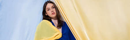 young ukrainian woman in color block clothing posing near blue and yellow curtains, bannerの写真素材