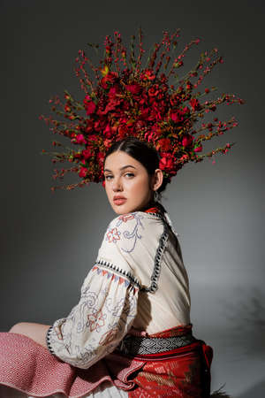 portrait of pretty ukrainian woman in traditional costume and floral red wreath on greyの写真素材