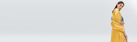 sensual young ukrainian model in blue and yellow dress posing while looking at camera isolated on grey, bannerの写真素材