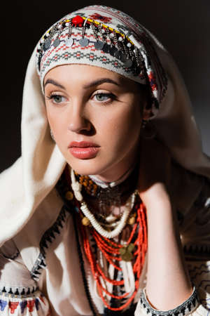 portrait of pensive young ukrainian woman in traditional clothing with ornament and red beads on...