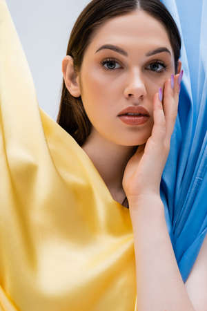 portrait of pretty and young ukrainian woman near blue and yellow fabric isolated on grey