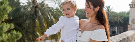Smiling mom holding baby pointing with finger on Puente Del Mar bridge in Valencia, banner