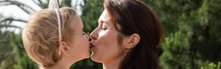 Side view of brunette mother kissing baby daughter outdoors in Valencia, banner
