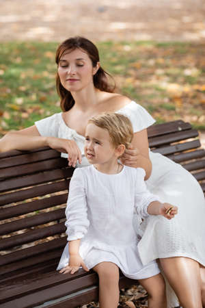 Toddler girl holding cookie near mom on bench in parkの写真素材