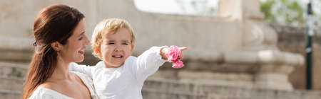 Brunette parent looking at baby daughter with flowers pointing with finger in Valencia, bannerの写真素材