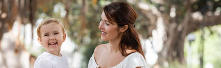 Cheerful baby girl laughing near mom in blurred park, banner