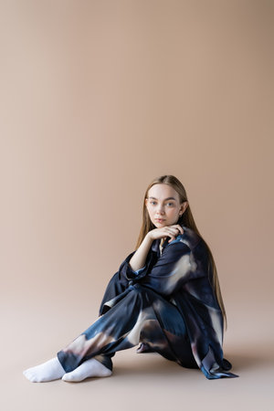 young woman in gradient clothing sitting with hand near chin on beige background