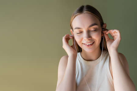 joyful woman with closed eyes listening music in wired earphones isolated on green