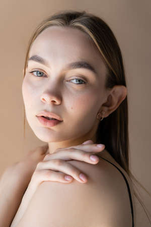 portrait of pretty woman with natural makeup hugging shoulders isolated on beigeの写真素材