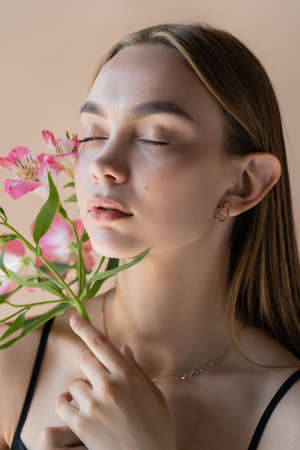sensual woman with closed eyes and perfect skin smelling alstroemeria flowers isolated on beigeの写真素材