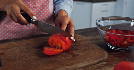 cropped view of woman cutting red tomato near bowl with chopped bell pepperの写真素材