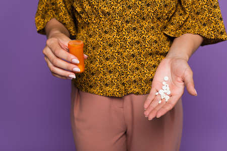 cropped view of woman with menopause holding bottle and pills isolated on purple