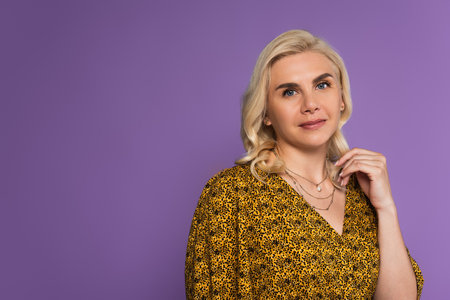portrait of joyful and blonde woman in blouse posing isolated on purple