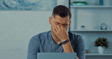tired freelancer touching eyes near laptop while working from homeの写真素材