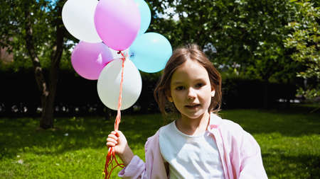 cheerful kid holding colorful balloons and looking at camera in green park