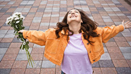 high angle view of happy woman holding white flowers and standing with outstretched handsの写真素材