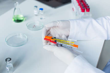 Cropped view of scientist holding syringes near vaccine and petri dishes in labの写真素材