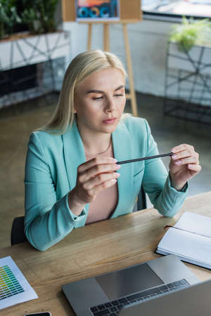 Psychologist holding pencil near laptop and notebook in consultation roomの写真素材
