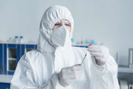 Scientist in hazmat suit and goggles holding syringe in laboratoryの写真素材