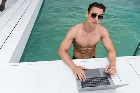 athletic man in sunglasses using laptop at poolsideの写真素材