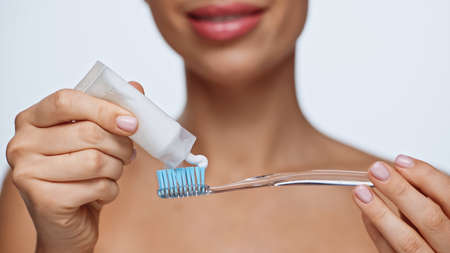 cropped view of cheerful young woman squeezing toothpaste on toothbrush isolated on white