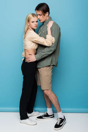 Full length of trendy young couple hugging on blue background