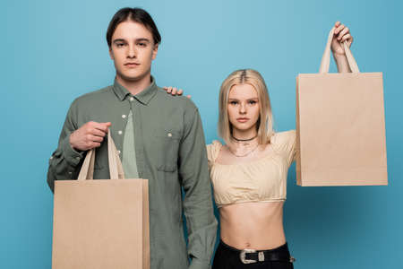 Pretty woman holding shopping bag and touching boyfriend isolated on blueの写真素材