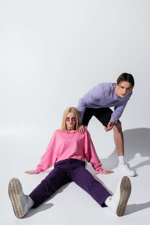 Blonde woman in pink sunglasses sitting near boyfriend on grey background