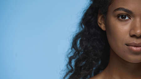 cropped view of brunette african american woman looking at camera isolated on blueの写真素材