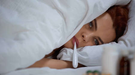 sick woman measuring temperature with electronic thermometer and lying on bed