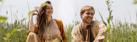 Positive couple sitting near grass in field, banner