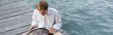 Man performing on hang drum on pier above river in Venice, banner