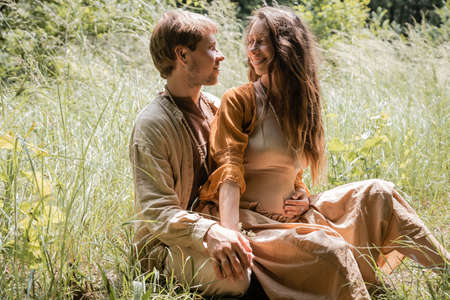 Smiling man hugging pregnant wife on grassy fieldの写真素材