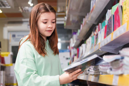 schoolgirl looking at new copybook near blurred rack in stationery shopの写真素材