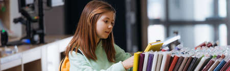 schoolgirl choosing from different notebooks in stationery shop, banner