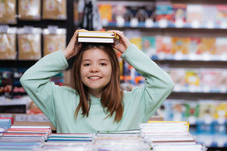 cheerful girl holding new notebooks above head and looking at cameraの写真素材