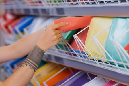 partial view of tattooed woman taking plastic folder from rack in stationery shop