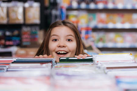 excited child looking at camera near blurred copybooks in stationery storeの写真素材