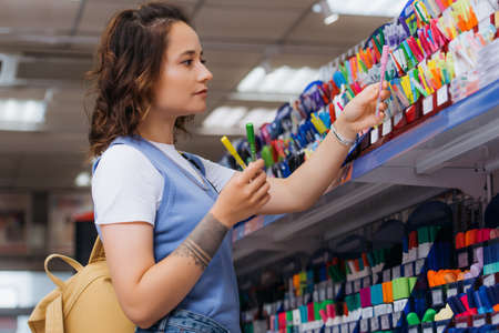 side view of tattooed woman holding multicolored pens near rack in shopの写真素材