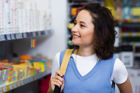 happy young woman with backpack near blurred rack with stationeryの写真素材