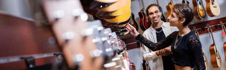 African american seller looking at woman choosing acoustic guitar in music store, bannerの写真素材