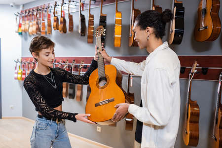 African american seller giving acoustic guitar to smiling customer in music storeの写真素材