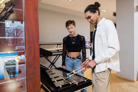 African american seller playing xylophone near customer in music store