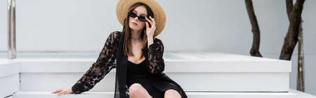Stylish woman in swimsuit and sun hat holding sunglasses near pool, bannerの写真素材